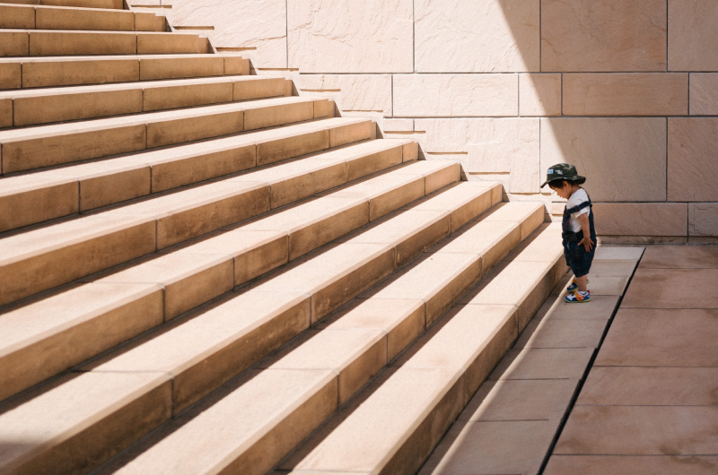 Zdjęcie przedstawia chłopca stojącego przy szerokich schodach.